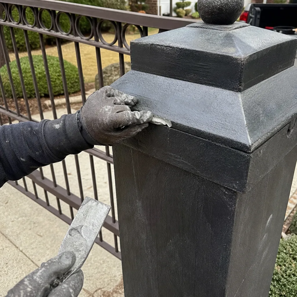 Repair technician patching a crack on an ornamental black metal gate post